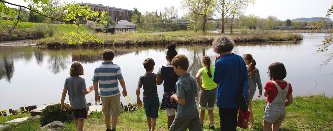 A group of students and a teacher standing next to the Campus Pond.