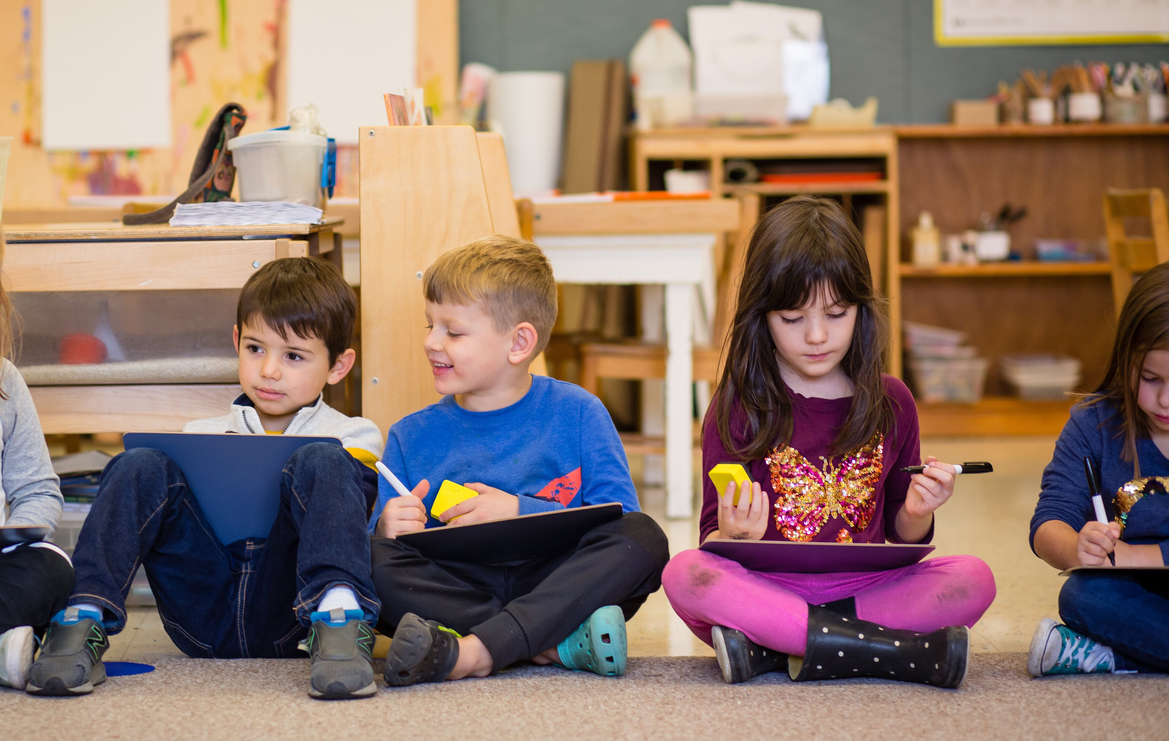 two kindergarten boys and two kindergarten girls sitting on the rug practicing handwriting