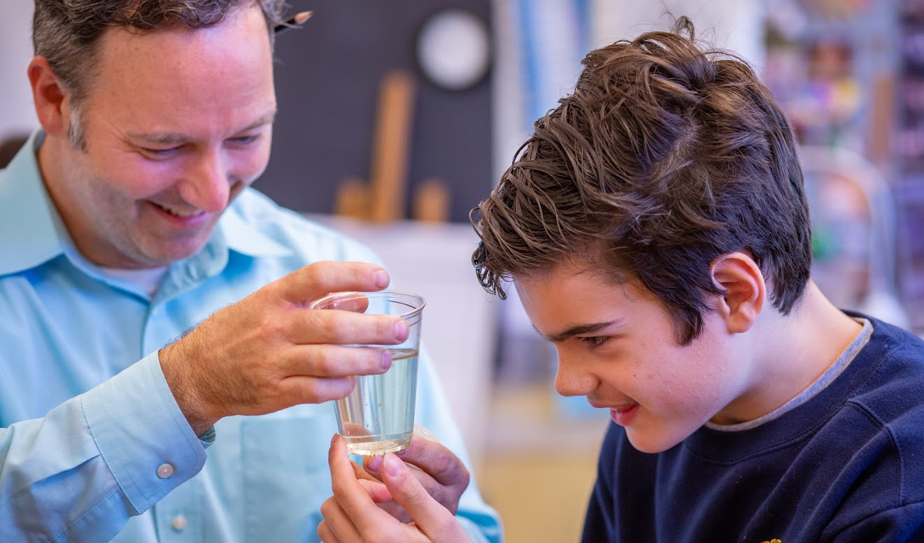 A student examining a cup of water with a teacher