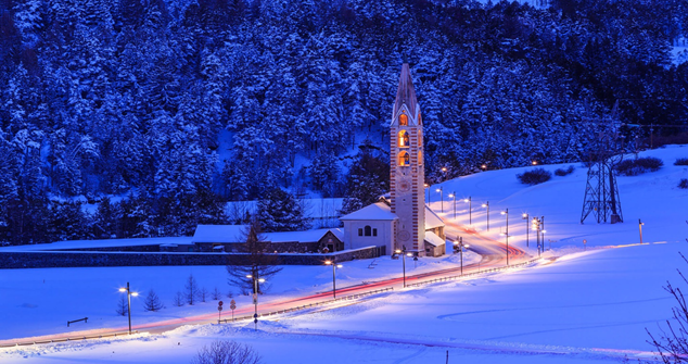 snowy night image of a street illuminated by street lamps